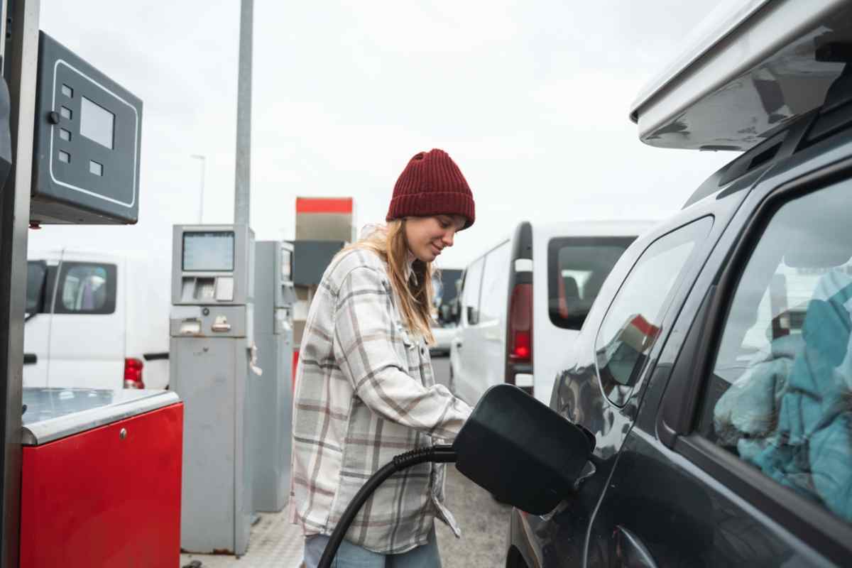 Traveler in a beanie refueling a car at a gas station.