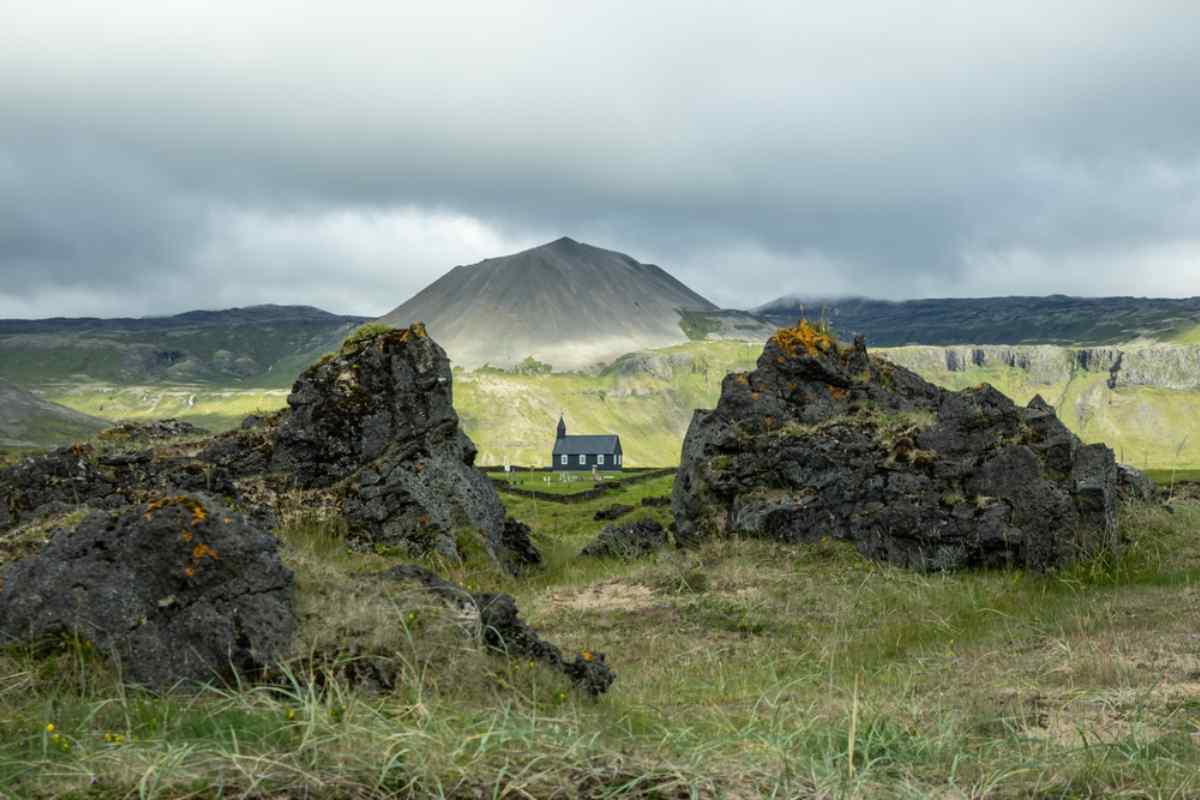 Snæfellsnes Peninsula Small black wooden church on Iceland’s Snæfellsnes Peninsula framed by jagged lava rocks and a conical volcanic mountain under low gray clouds.