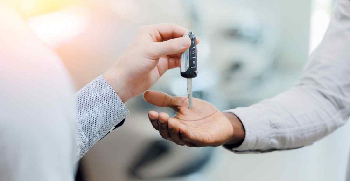 Renting a car in Iceland Close-up of a car rental handover, with one person passing a modern car key into another person’s open palm inside a bright showroom.