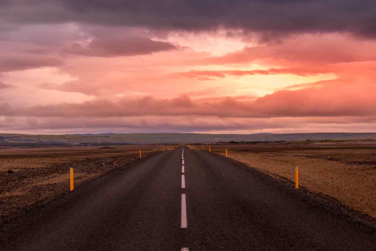 Driving around Iceland under the Midnight Sun Straight Icelandic road stretching toward the horizon under a dramatic pink and orange sunset sky, with open barren landscape on both sides.