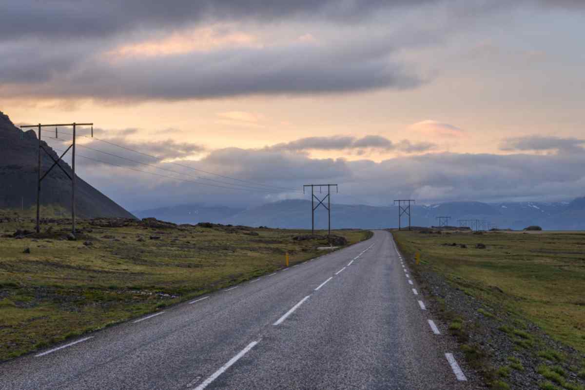 General view of an Icelandic asphalt road with light poles in the road during sunset.