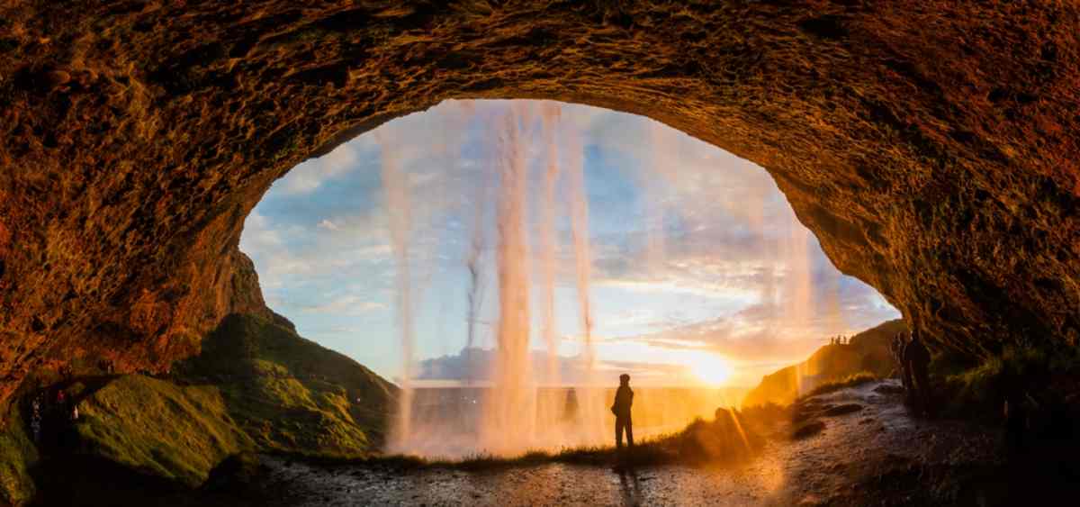 Tourist standing behind a waterfall during the sunset