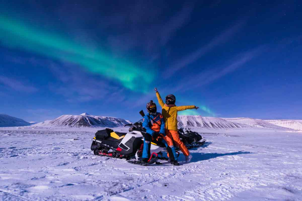 Northern lights over a couple of snowmobile drivers