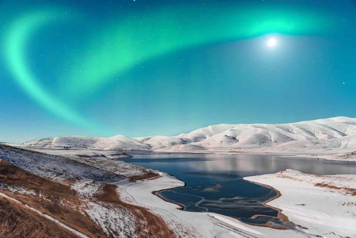 Northern lights dancing on top of snowed hills in Iceland