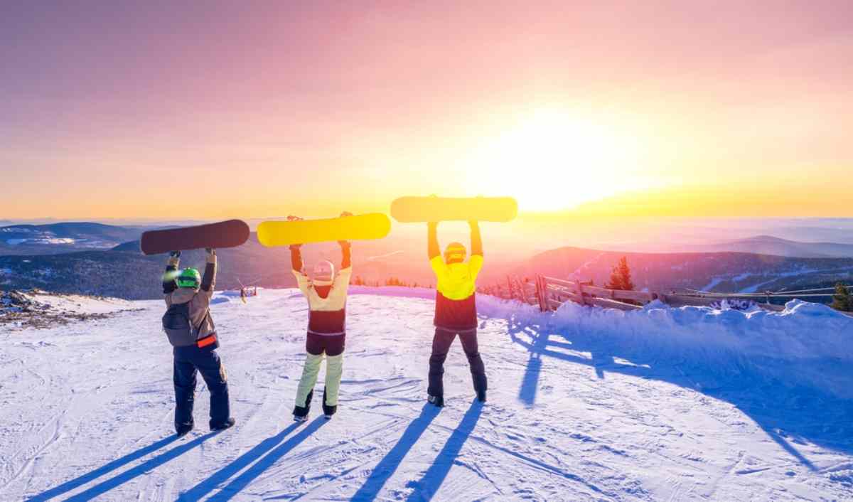 Trio of snowboarders holding their board against the sun