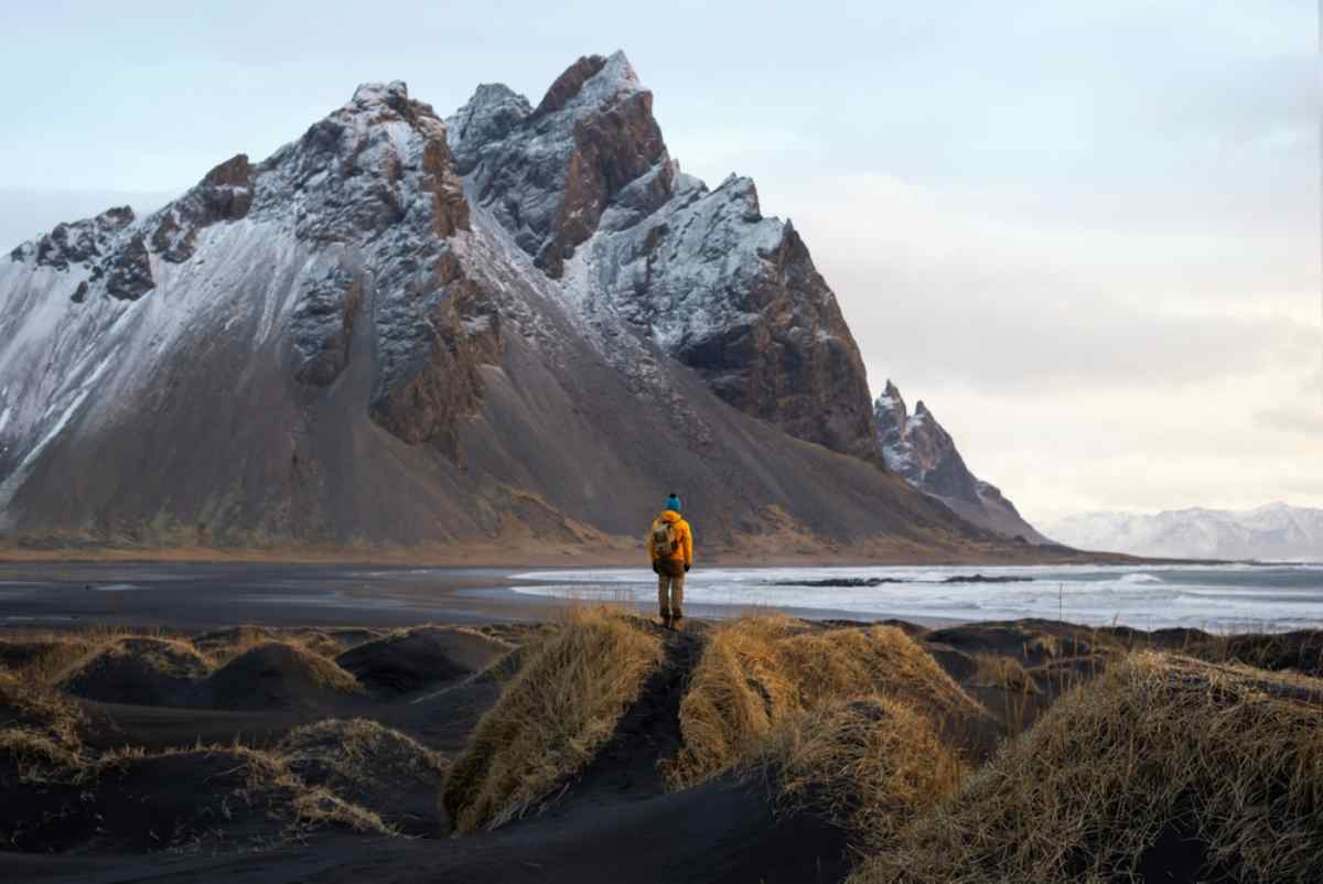  tourist stands on the beach, admiring the majestic reflection of the Vestrahorn mountain