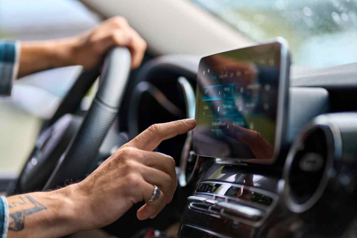 A finger points to a smartphone screen clutched to the dashboard of a car in what appears to be an attempt to connect the GPS.