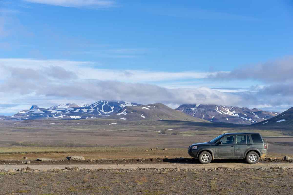 Renting a 4x4 in Iceland A 4x4 vehicle is parked on the right side of what looks like a postcard of a winding unpaved Icelandic road.