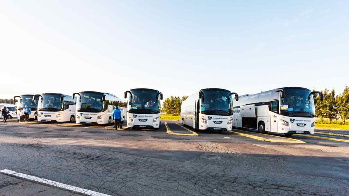 Public buses in Reykjavik A row of buses remain parked in a Reykjavik parking lot while several men from outside stand next to them.