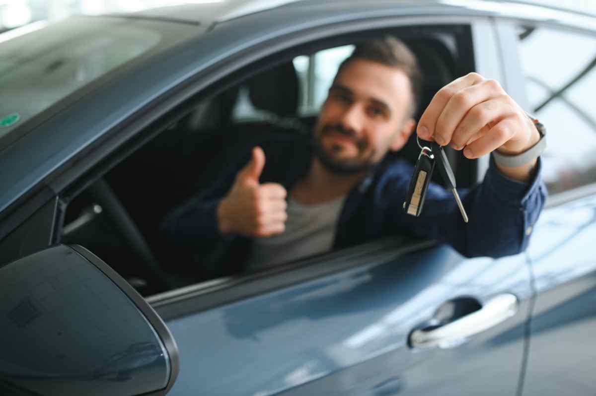 The importance of getting a rental car A happy man holds a set of car keys while sitting in the driver's seat of a car with the window down.
