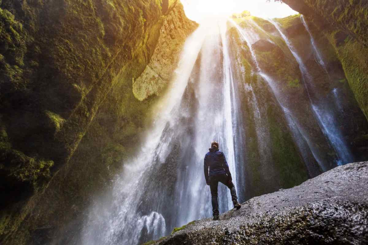 Close-up of a man standing just below the Glj&uacute;frab&uacute;i waterfall as the sun's rays fall on it
