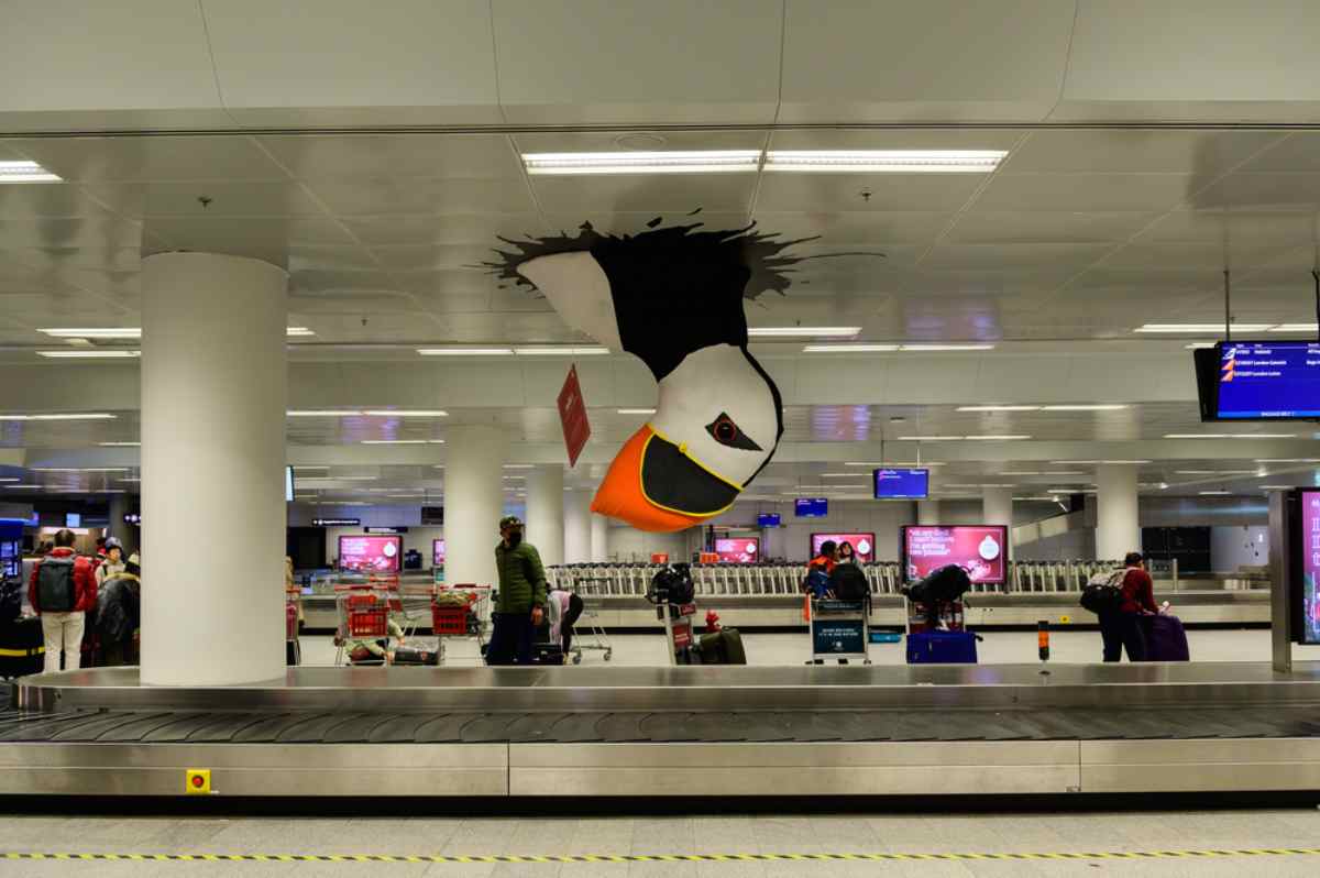 Image from Keflavik airport showing a group of people in the luggage reclaim next to what looks like an inflatable puffin sticking out of the ceiling.