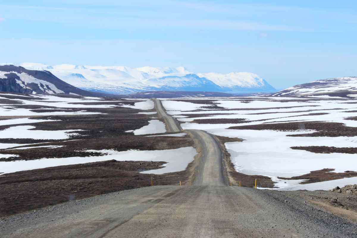 General view of a kilometer-long road in Iceland surrounded by snow-capped mountains.