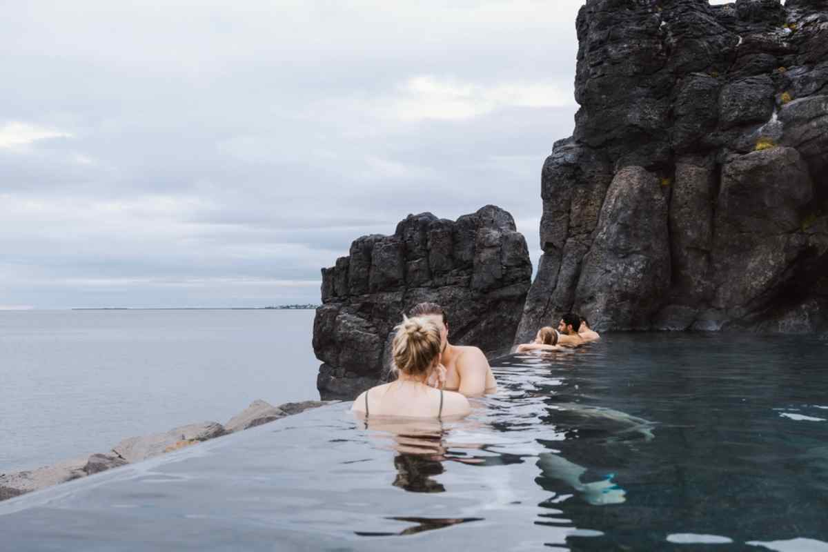 A group of people take a swim in Iceland's Sky Lagoon surrounded by black rocks