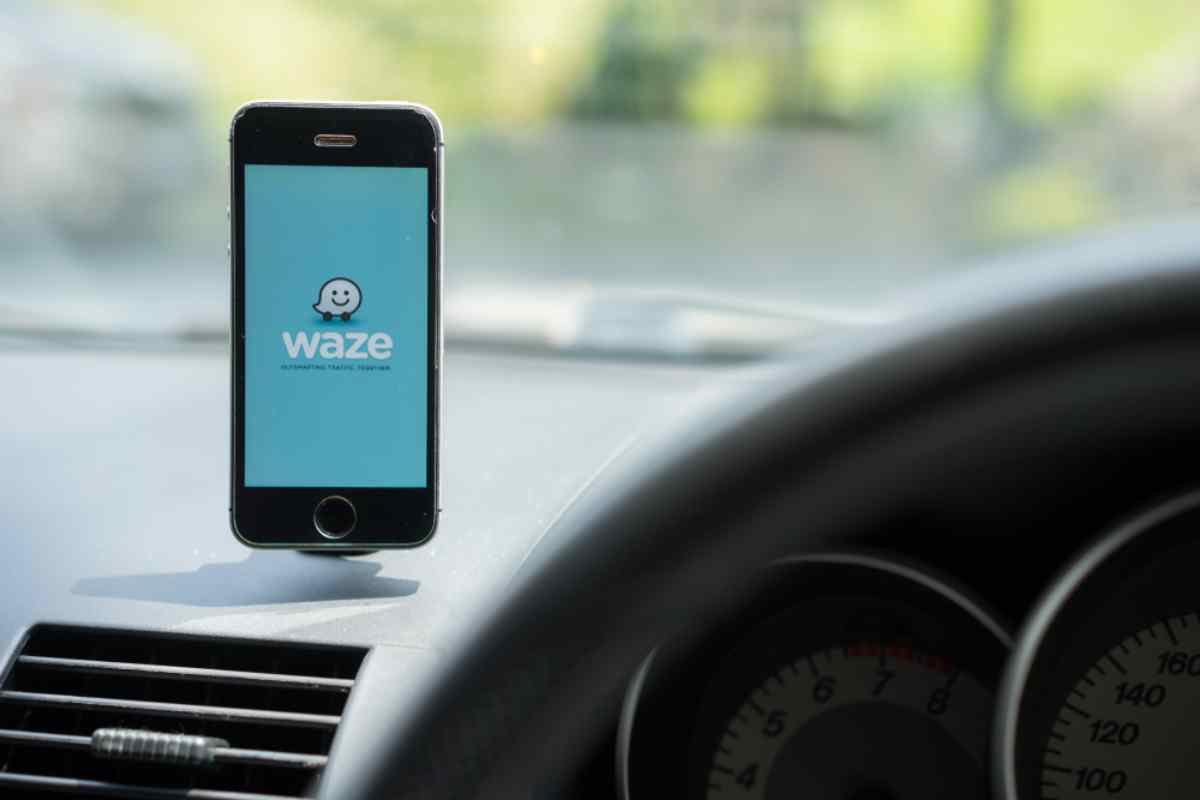 A cell phone attached to a car window displays the logo of the GPS application Waze.