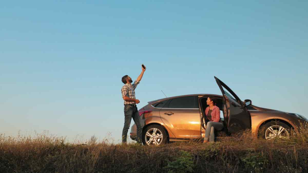 A couple stranded on the road tries to find signal outside their parked vehicle.