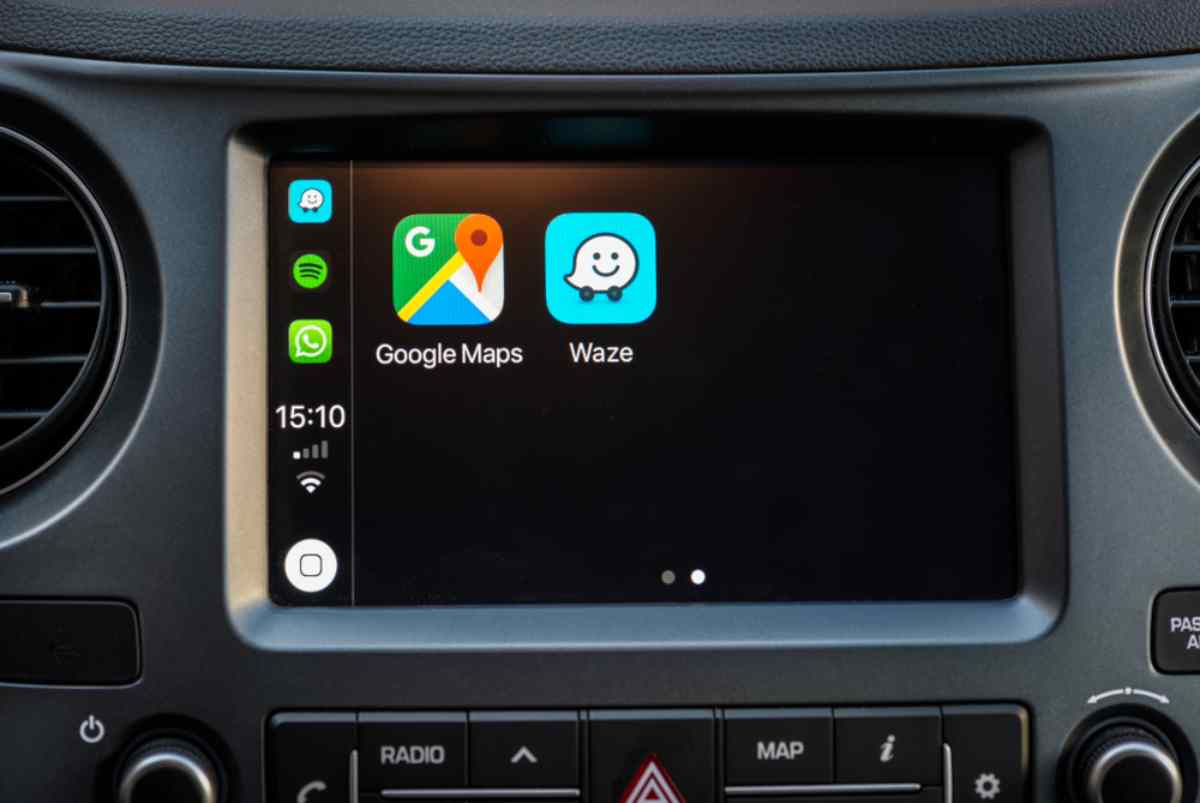 A small screen of a vehicle displays the logos of the GPS apps Google Maps and Waze.