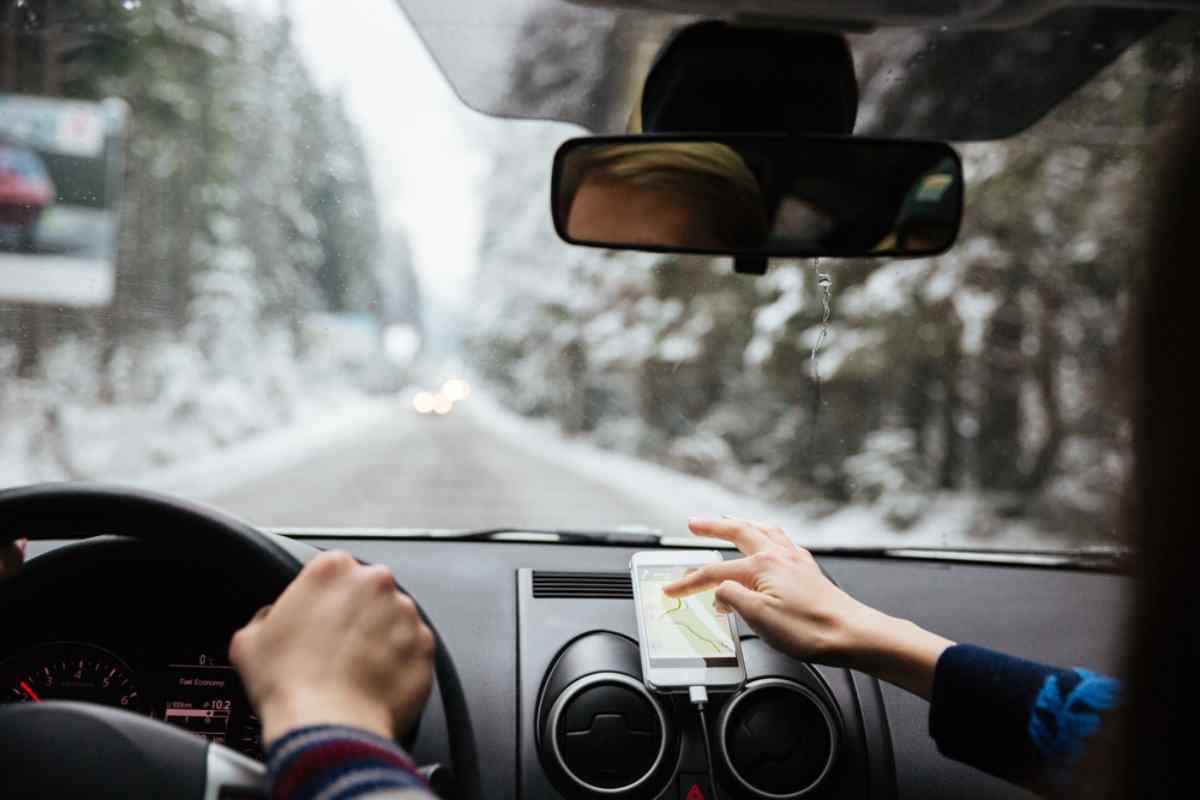 A couple remains in the front seats of a moving vehicle while the occupant of the passenger seat manipulates a cell phone screen in what appears to be an attempt to connect the cell phone's GPS.