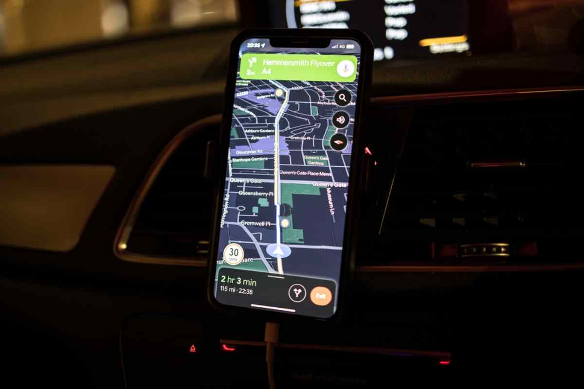 A cell phone screen clinging to the dashboard of a moving car displays an interactive map in the Icelandic night.
