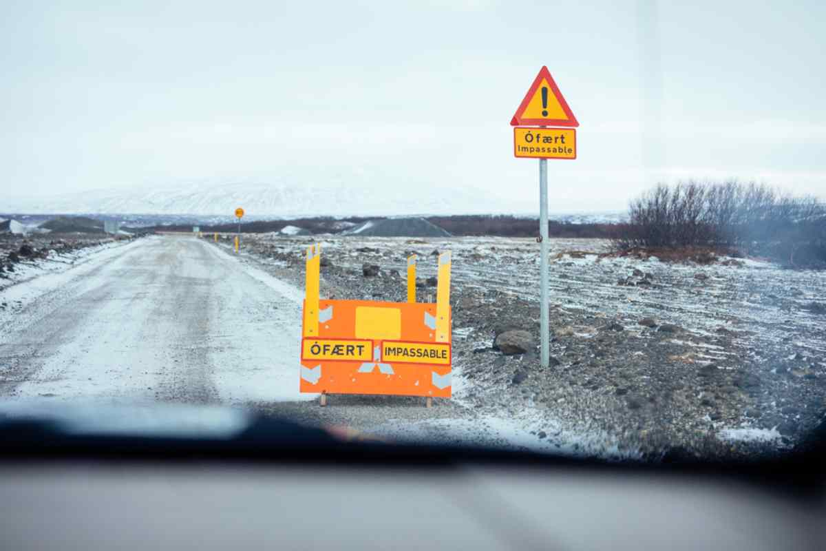 A road sign with inscription in local language and English indicates the prohibition of access to a road due to its closure.