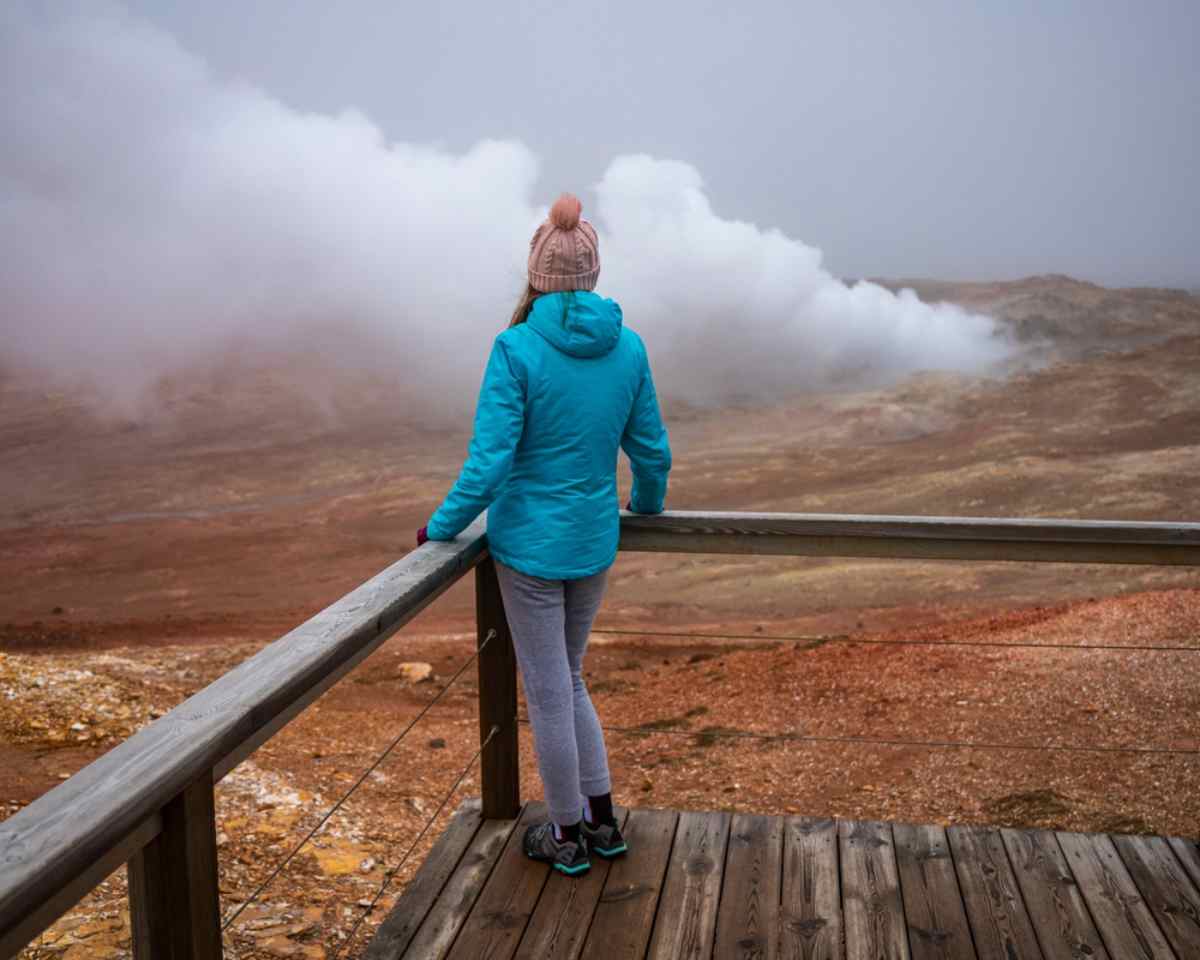 A woman in warm clothes looks straight ahead at the Gunnuhver hot springs.
