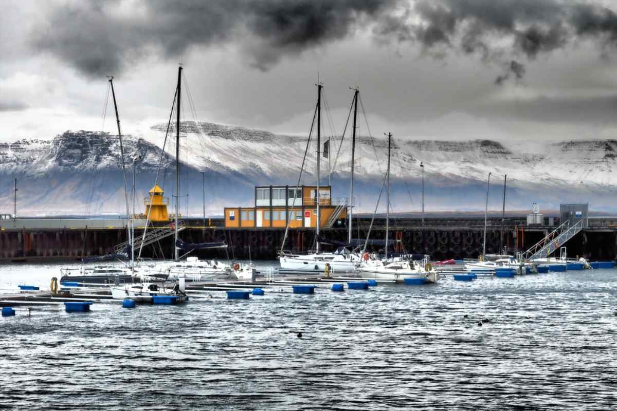 General view of Reykjavik's old harbor on a cloudy day with several ships moored at the pier and snow-capped mountains in the background.