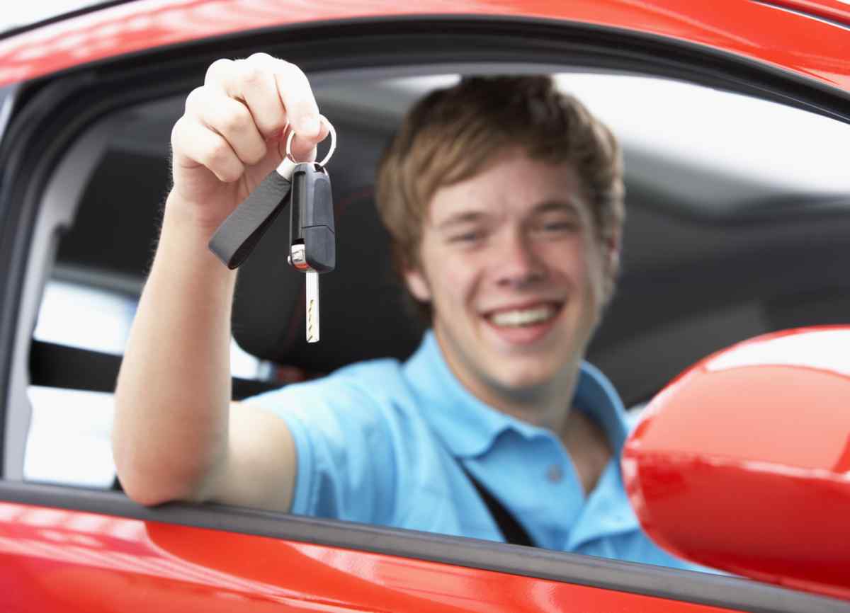 A young blond boy holds a flame from a car while sitting in the driver's seat of a car.