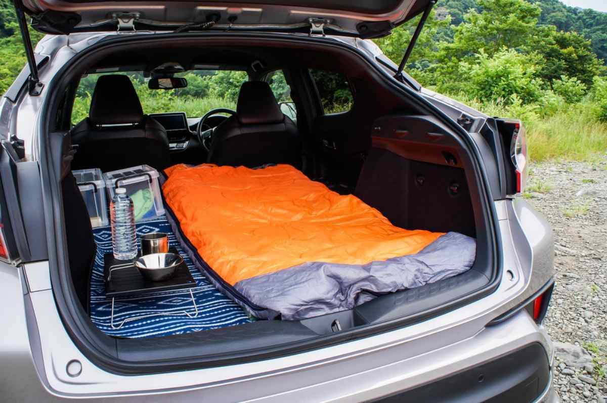 Overview of an open trunk, equipped for overnight stays, with an unfolded sleeping bag and various cooking utensils.