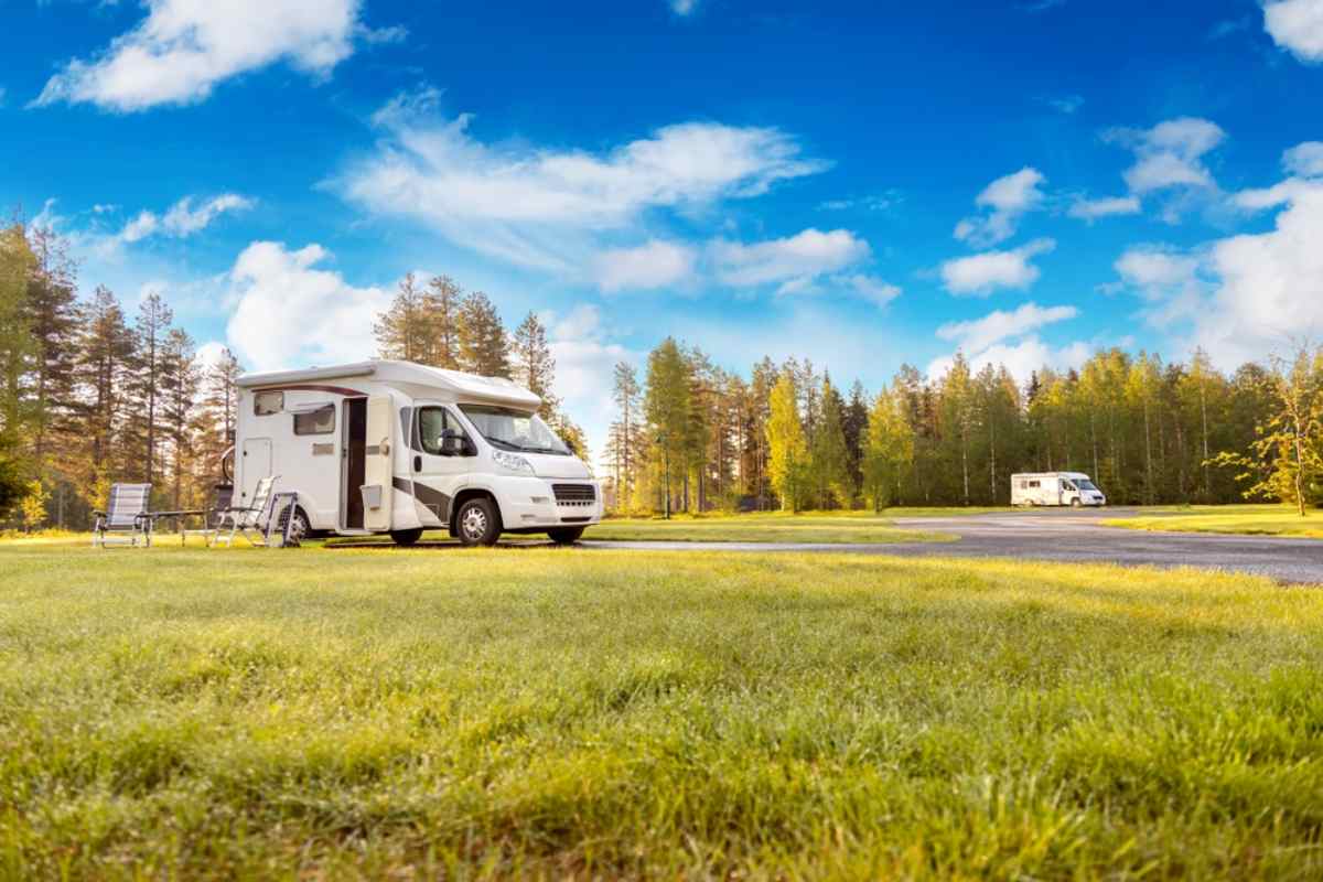 Overview of a campground with several motorhomes parked several meters apart in what appears to be a forest on a sunny day.