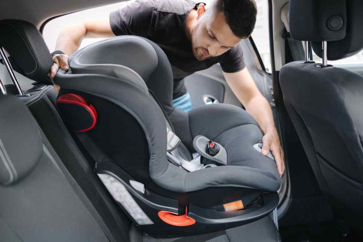 A man tries to place a kid car seat in the back of a car from one of the open doors.