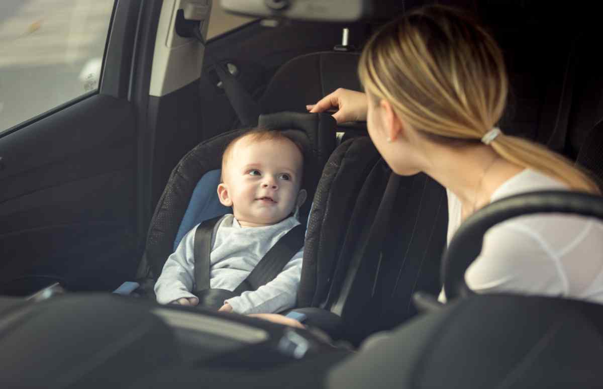 A woman observes from the driver's seat her baby in a car seat in the front passenger seat.