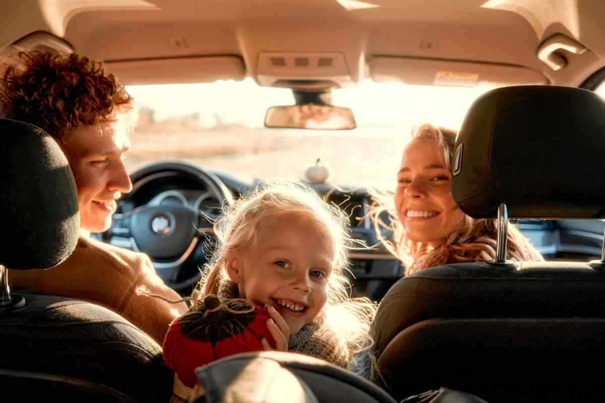 Smiling family inside a car during a road trip, with a young girl looking back from the front seat Icelandic family on the road