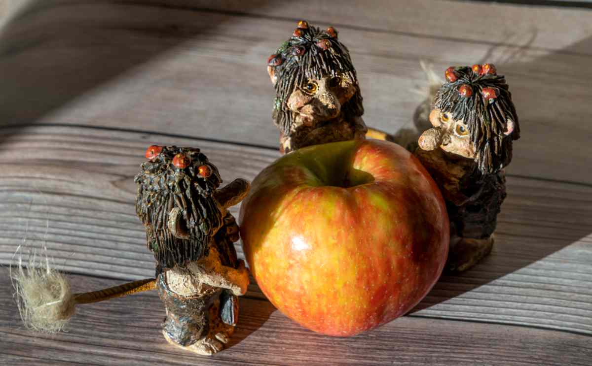 Three small troll figurines from Icelandic folklore gathered around a red apple on a wooden surface Icelandic folklore