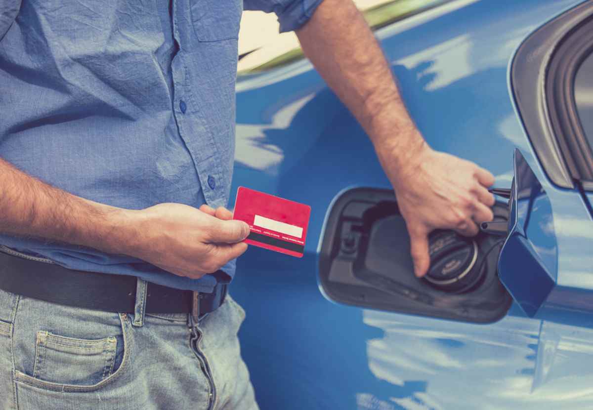 Man holding a credit card while refueling a blue car at a gas station in Iceland.