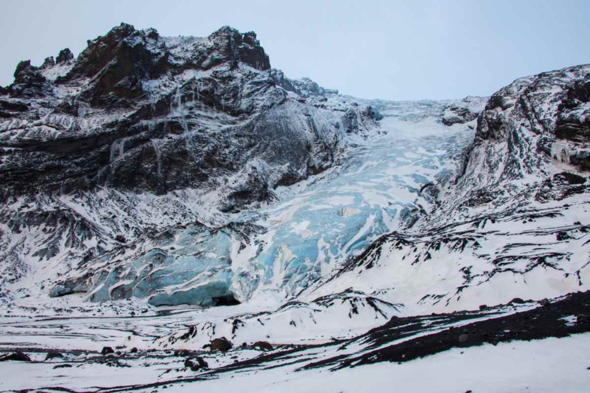 Gigjokull Glacier Blue ice tongue of Gigjokull glacier below dark volcanic cliffs, seen from the F249 area in South Iceland during winter snowfall and overcast light.