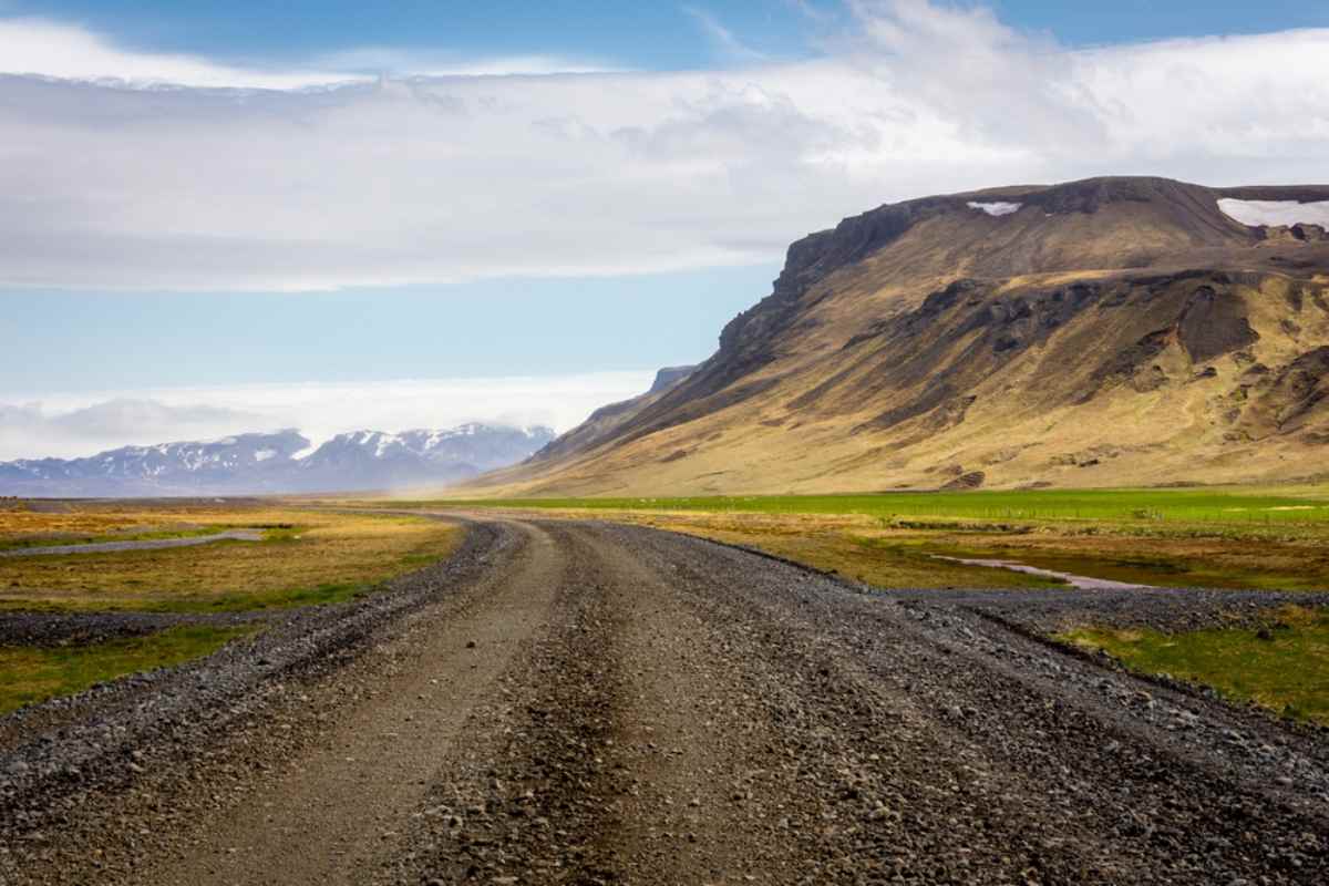 Where is the F249 road in Iceland? Curving gravel road across an open South Iceland valley leading toward a flat-topped mountain, with pasture greens and far snow-dusted peaks.