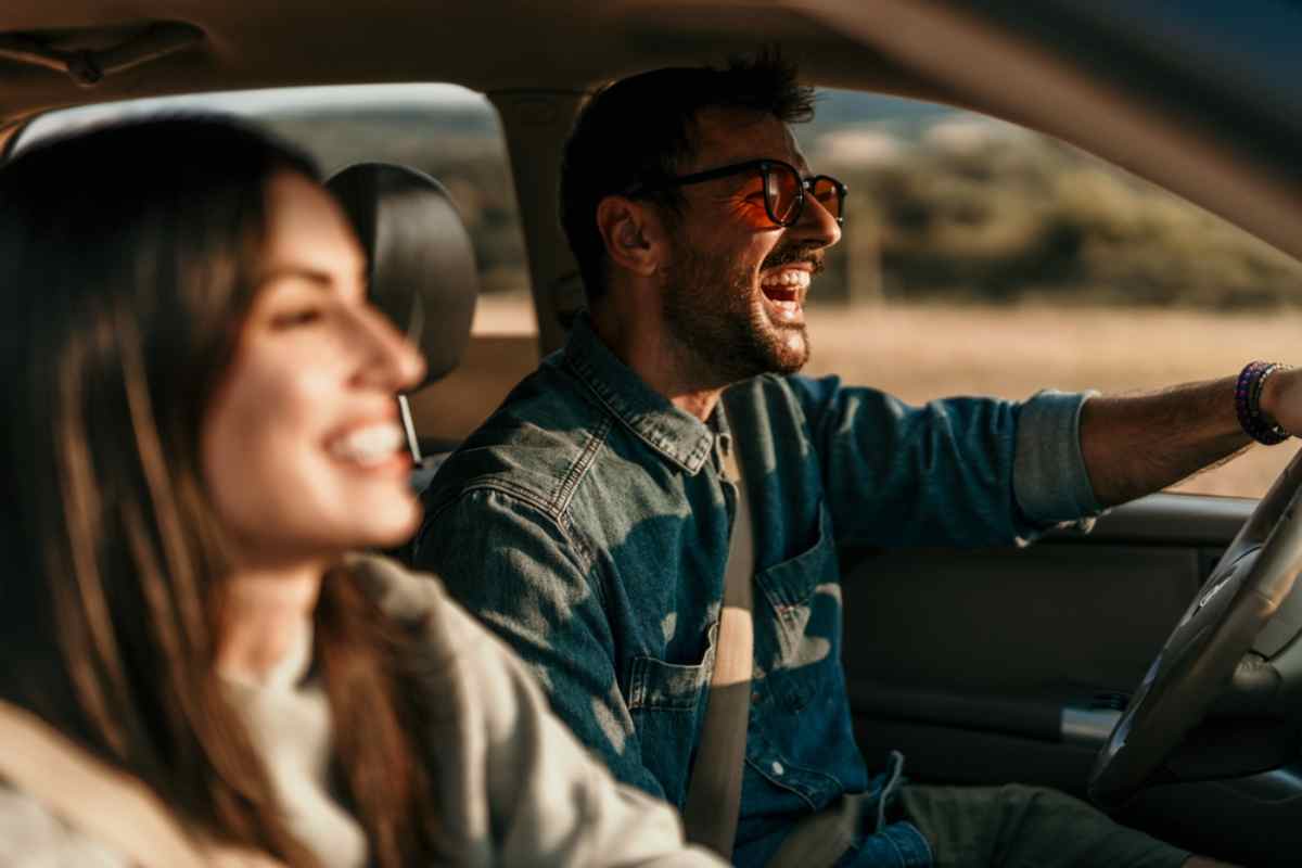 Smiling couple on an Iceland road trip, with the driver laughing behind the wheel of a rental car.