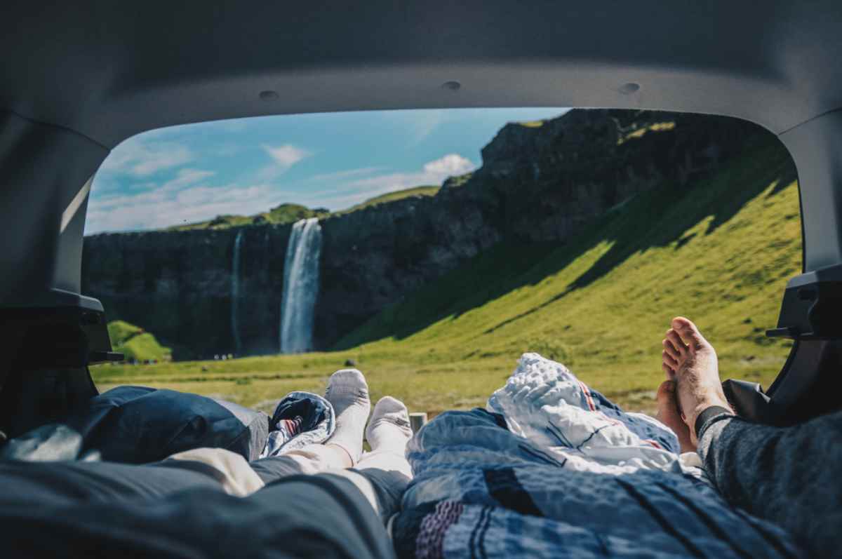 Exploring Iceland without crowds View from a car’s open hatch—feet and sleeping bags framing a waterfall in Iceland.