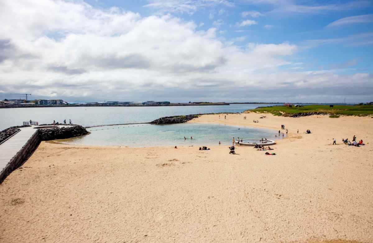Nauth&oacute;lsv&iacute;k geothermal beach in Reykjavik, with a sandy lagoon, people relaxing, and calm coastal views.