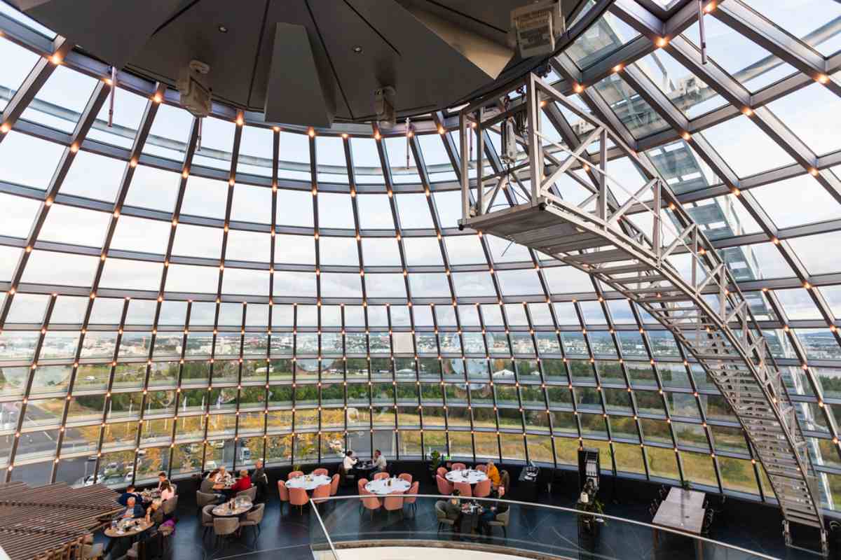Inside the Perlan observation deck in Reykjavik, a glass dome with panoramic city views, stairs, and caf&eacute; seating.