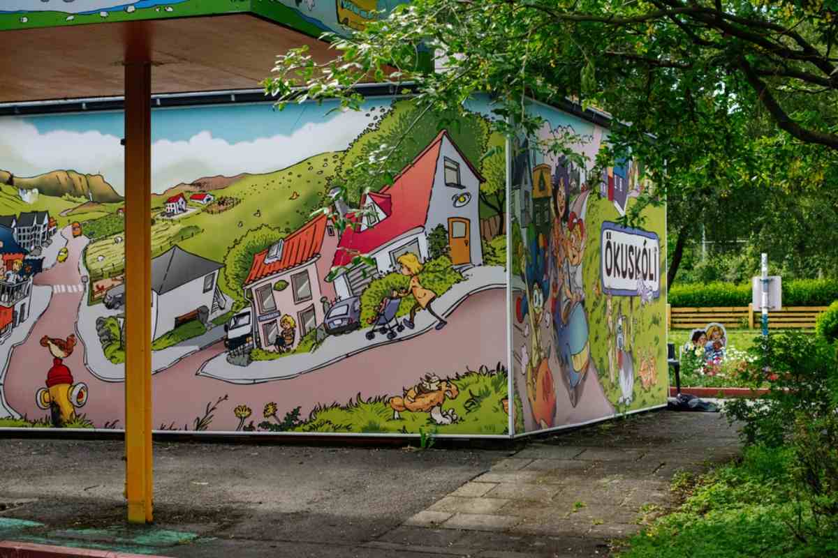Colorful Reykjavik street art mural painted on a building wall, with trees and a small park area nearby.