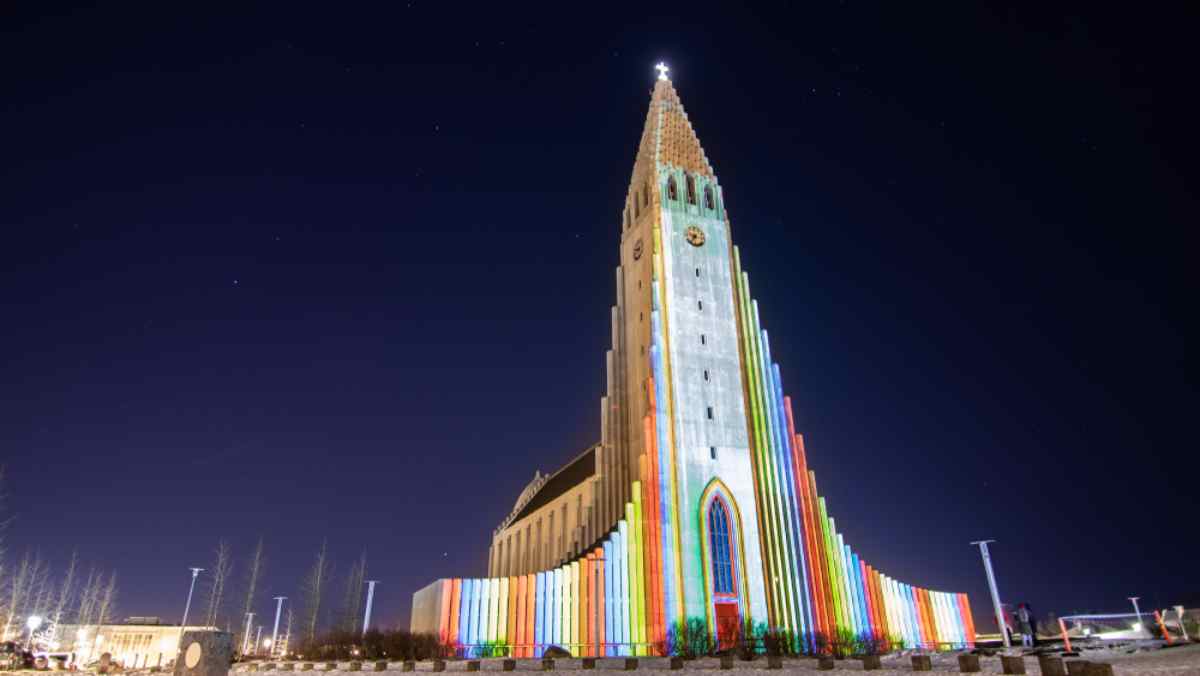 Hallgr&iacute;mskirkja church in Reykjavik glowing with rainbow projections during the Winter Lights Festival, set against a dark sky.
